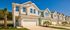 Modern townhouses with elegant design, featuring bright exteriors, welcoming entrances, and lush landscaping under a clear blue sky.