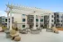 Outdoor courtyard at a modern apartment community featuring comfortable lounge seating, dining tables, and recreational amenities with contemporary apartment buildings in the background.