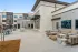 Outdoor courtyard at a modern apartment community featuring comfortable lounge seating, dining tables, and recreational amenities like a ping pong table, with contemporary apartment buildings in the background.