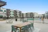 Outdoor courtyard at a modern apartment community featuring comfortable lounge seating, dining tables, and recreational amenities like a ping pong table, with contemporary apartment buildings in the background.