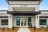 Front entrance of a modern apartment community clubhouse with white siding, black trim, double glass doors, and a sign reading &lsquo;CLUB&rsquo; above the entryway