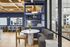 Contemporary shared lounge space featuring elegant blue shelving, chic marble table, and stylish seating under wooden beam ceiling.