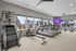 Modern apartment gym with state-of-the-art equipment, large windows for natural light, and a lively outdoor view.