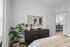 Chic bedroom with modern decor, elegant dresser, large mirror, and view into a stylish open kitchen.