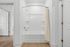 Elegant bathroom featuring a pristine white bathtub with a modern design and stylish beige shower curtain, adjacent to sleek wooden flooring.