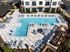 Aerial view of a luxurious apartment complex featuring a stunning geometric pool with sun loungers, shaded tables, and lush landscaping.