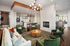 Chic modern living room with elegant furniture, vibrant green armchairs, stylish chandelier, and cozy fireplace adjacent to an open kitchen.