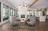 Luxurious, modern lounge area with elegant armchairs, stylish chandelier, and cozy fireplace; open-concept design leading to a sleek kitchen with high-end finishes.