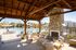 Inviting outdoor space featuring a cozy stone fireplace under a wooden pergola, overlooking a sparkling pool with comfortable lounge chairs.