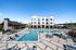 Luxurious apartment complex showcasing a sparkling swimming pool, stylish lounge chairs, and modern architecture under a clear blue sky.