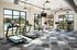 Modern fitness center with sleek treadmills and stationary bikes, featuring large windows and a stylish geometric carpet pattern, offering a refreshing view of the outdoor pool and greenery.