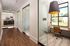 Elegant modern office hallway with glass-walled rooms and stylish wood flooring, featuring abundant natural light from large windows.