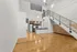 Modern open-plan apartment with sleek kitchen, polished hardwood floors, and an elegant staircase leading to a loft area.