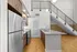 Modern apartment kitchen with sleek stainless steel appliances, elegant wooden cabinetry, and a stylish granite countertop, next to an open staircase and a spacious hardwood floor area.