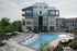 Modern apartment complex featuring a luxurious poolside area with stylish lounge chairs, elegant sun umbrellas, and lush greenery, promising a resort-like living experience.