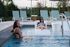 Serene outdoor pool area with smiling guests enjoying relaxation on loungers, surrounded by lush greenery.