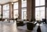 Modern lounge area with high ceilings, brick walls, large windows, and stylish furnishings, featuring a chic pool table and cozy seating arrangements.