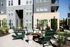 Modern outdoor patio space with elegant fire pit surrounded by stylish green Adirondack chairs, set against a chic apartment building backdrop, perfect for relaxation and social gatherings.