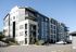 Modern residential apartment building with multiple balconies, surrounded by lush greenery and ample parking space.