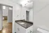 Pristine bathroom with modern fixtures, granite countertop, and spacious mirror adjacent to a bright hallway with wooden floors.