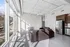 Sunlit modern apartment with large windows, sleek brown leather couches, and stainless steel kitchen appliances.