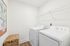 Modern laundry room featuring a sleek washer and dryer, wicker storage basket, and elegant wall art, complemented by clean white walls and wooden flooring.