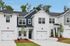 Charming modern townhouse with sleek white brick exterior, double garage doors, and lush landscaping under a clear blue sky.