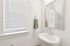 Bright and airy bathroom with sleek white fixtures, elegant oval mirror, and soft natural light streaming through blinds.