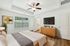 Bright and inviting bedroom featuring cozy bed, modern ceiling fan, large window with scenic view, and stylish wooden dresser with TV.