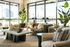Inviting modern living room with lush green plants, cozy seating, and large sunlight-filled windows.