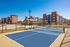 Modern apartment complex with sleek architecture and a sunlit blue tennis court surrounded by green landscaping.