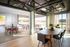 Bright and modern living space with an open layout, featuring sleek dining tables and abundant natural light through large windows.