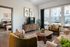 Modern living room with chic decor, featuring stylish furniture, abundant natural light from large windows, and a cozy adjacent bedroom view.