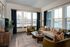 Charming living room with large windows, cozy beige sofa, stylish green armchairs, and elegant decor creating a warm, inviting atmosphere.