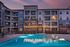 Elegant apartment complex with a sparkling pool and ambient string lights at dusk.