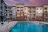 Luxurious apartment complex featuring a stunning outdoor pool area with lounge chairs, set against a beautifully designed multi-story building under a vibrant evening sky.