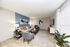 Modern living room with elegant decor, featuring a stylish gray sofa, blue accent chairs, artistic wall paintings, and a large window providing natural light.