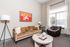 Chic living room with a cozy beige sofa, vibrant artwork, elegant floor lamp, and large window welcoming natural light.