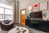 Contemporary living room with elegant decor, featuring a leather armchair, stylish media console with a flat-screen TV, and vibrant wall art next to a large window with natural light.