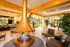 Luxurious living area showcasing a modern suspended fireplace with vibrant decor, elegant seating, and expansive windows offering lush garden views.