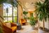 Bright and inviting living area with lush indoor plants, elegant orange chairs, and floor-to-ceiling windows offering natural light and scenic views.