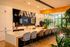 Luxurious modern kitchen with sleek countertops, stylish chairs, and elegant lighting, surrounded by lush greenery and large windows.