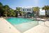 Luxurious apartment complex with a stunning pool, surrounded by lush palm trees and modern lounge areas under bright blue skies.