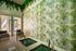 Inviting indoor space with a vibrant plant-themed wall, relaxing seating, and a serene pool entrance, offering a refreshing tropical ambiance.