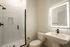 Modern bathroom with sleek glass shower, elegant illuminated mirror, and contemporary fixtures.