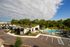 Inviting apartment complex with modern architecture, lush greenery, and a sparkling outdoor pool area under a bright blue sky.