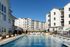 Luxurious apartment complex featuring a sparkling pool, modern architecture, and sun loungers under clear blue skies.