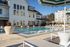 Luxurious apartment complex with a stunning swimming pool area, elegant loungers, and modern architecture set against a clear blue sky.