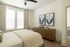 Inviting bedroom with soft natural light, featuring elegant decor, wooden dresser, and stylish botanical artwork.