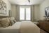 Cozy bedroom with a chic decor, featuring a plush bed with layered cushions, elegant artwork, and an inviting lounge chair by the window.